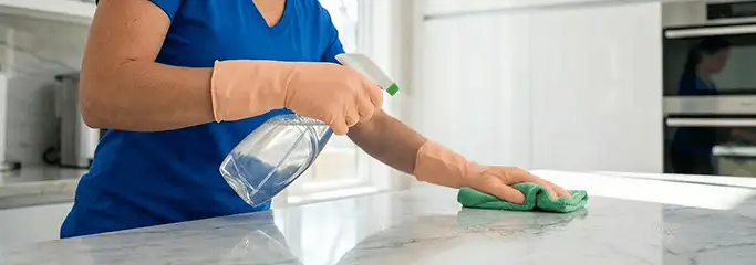 Maid service worker spraying and wiping a kitchen countertop with a microfiber cloth for sanitizing, Philadelphia, PA.