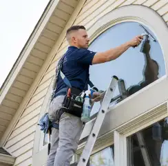 Professional window cleaner on a ladder using a squeegee to clean an exterior arched window, Philadelphia, PA.