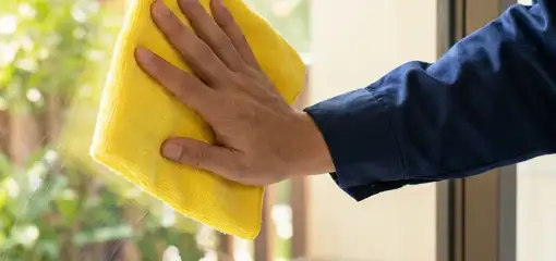 House cleaner wiping a glass window with a yellow microfiber cloth for streak-free cleaning, Philadelphia, PA.